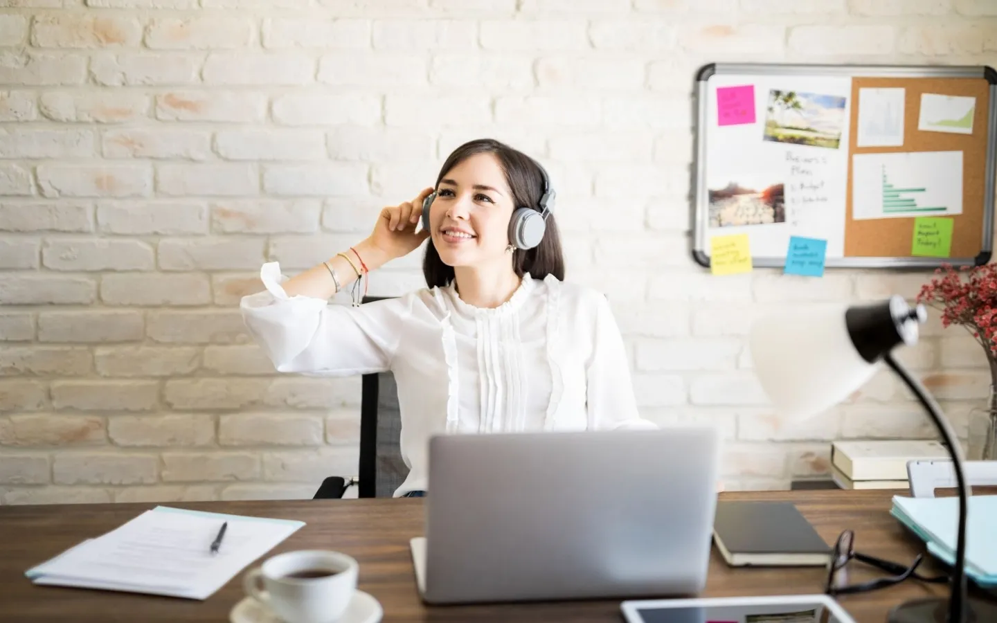Une femme ajuste son casque audio devant son ordinateur portable, une tasse de café posée à côté d'elle.