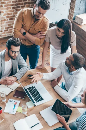 Une équipe réunie autour d'une table de travail échange en se serrant la main.