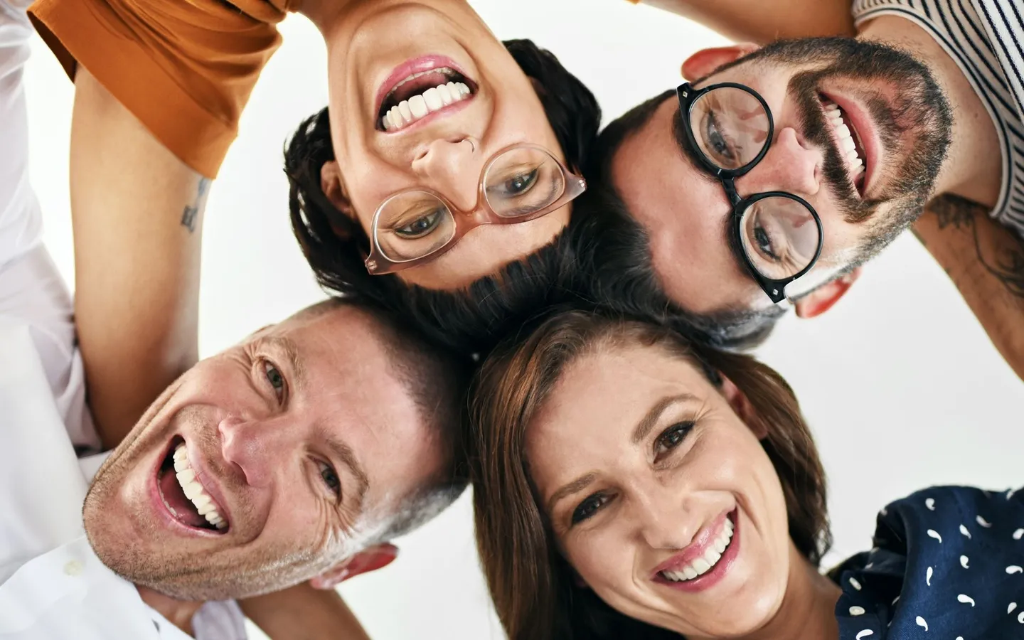 Quatre collègues réunis en cercle, vus de dessus, tête contre tête, le sourire aux lèvres.