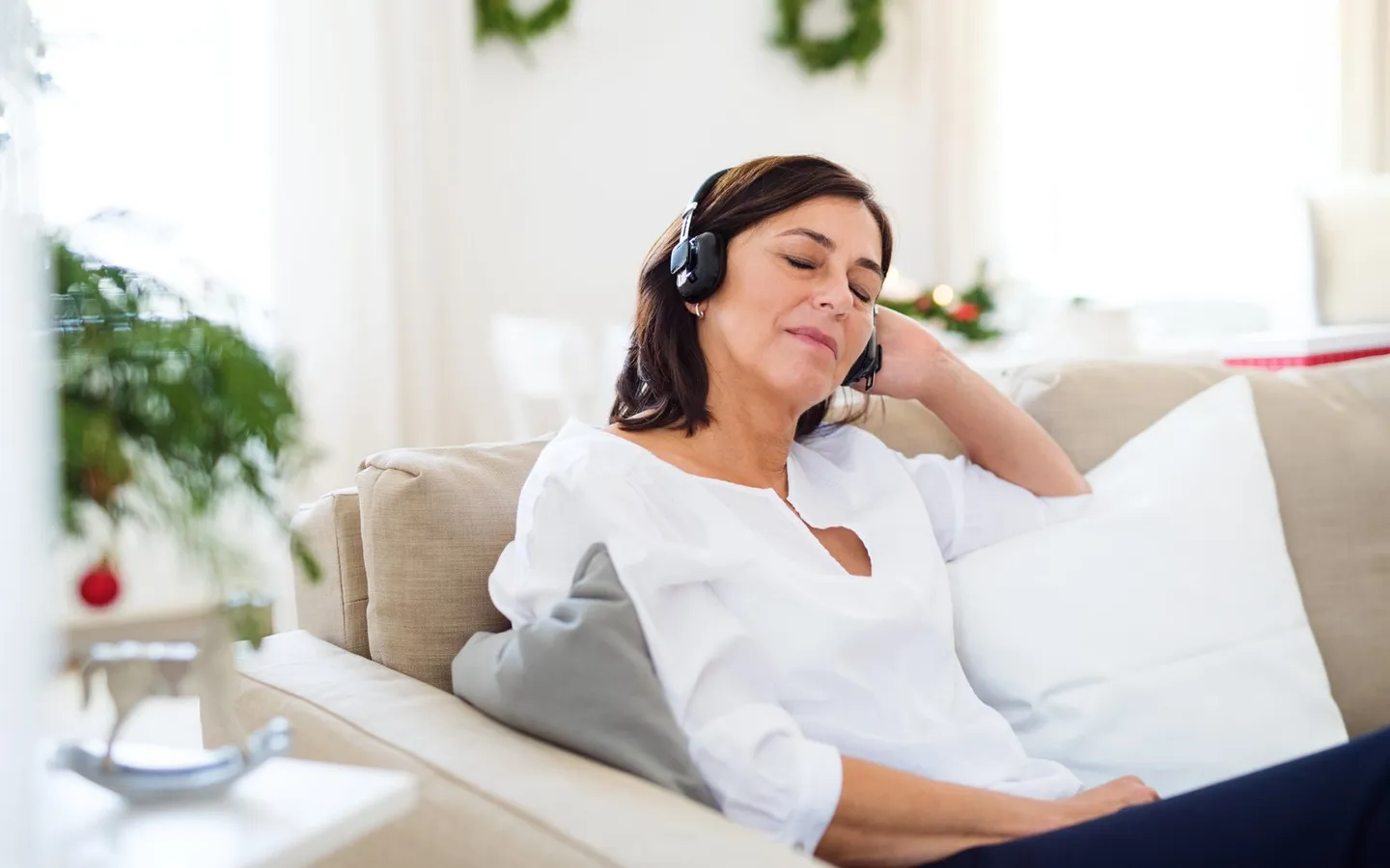 Une femme allongée sur un canapé clair, un casque audio sur les oreilles, les yeux fermés.