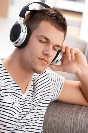 Un étudiant écoute au casque, les yeux fermés, détendu sur un canapé.