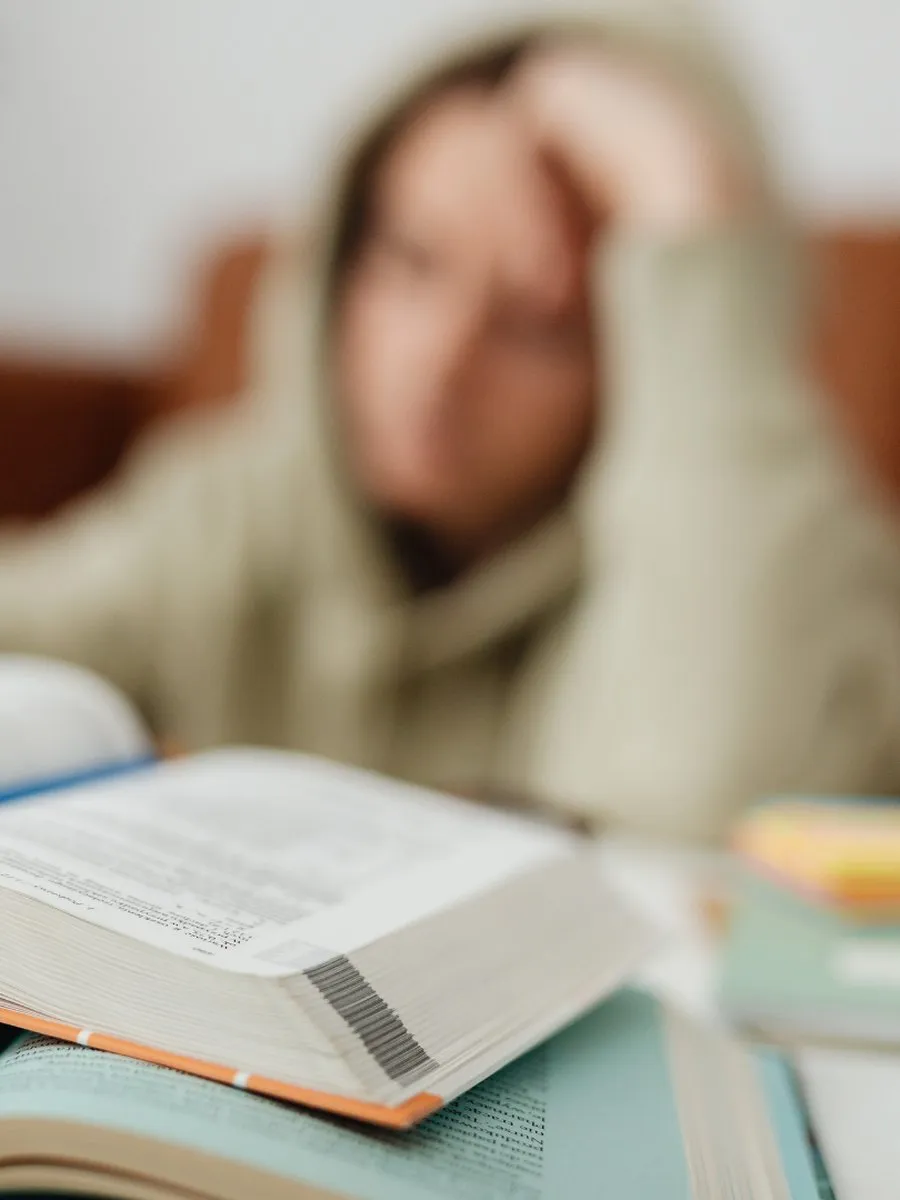 Une étudiante, la tête dans les mains, devant un livre ouvert et une pile de manuels.