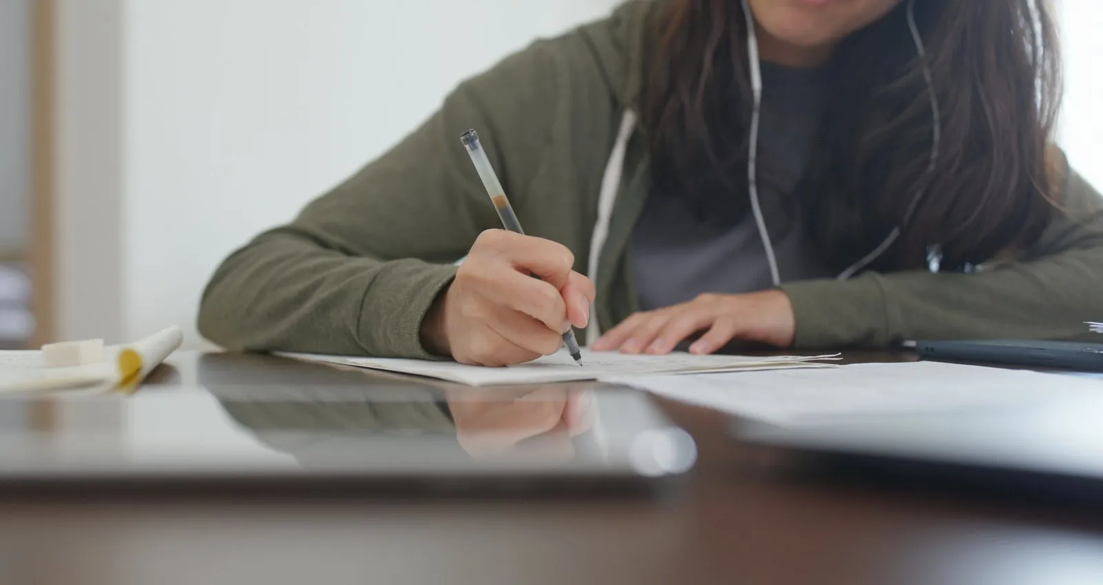 Une étudiante écrit sur une feuille, des écouteurs aux oreilles.