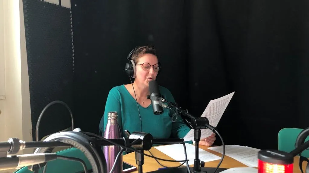 Marie-Laure Bourgeois au micro d'un studio d'enregistrement, casque sur les oreilles, lisant un texte qu'elle tient à la main.