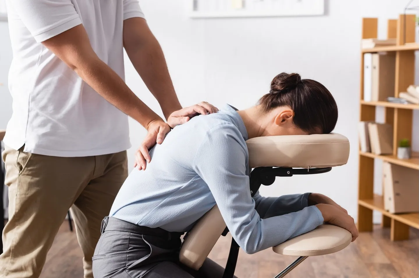 Une personne installée sur une chaise de massage assis, dans un bureau, pendant qu'un praticien lui masse le dos.