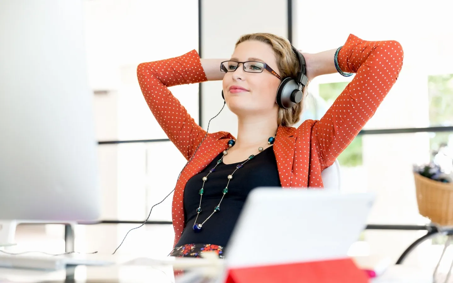 Une femme au casque audio s'étire, les bras derrière la tête, devant son écran de bureau.