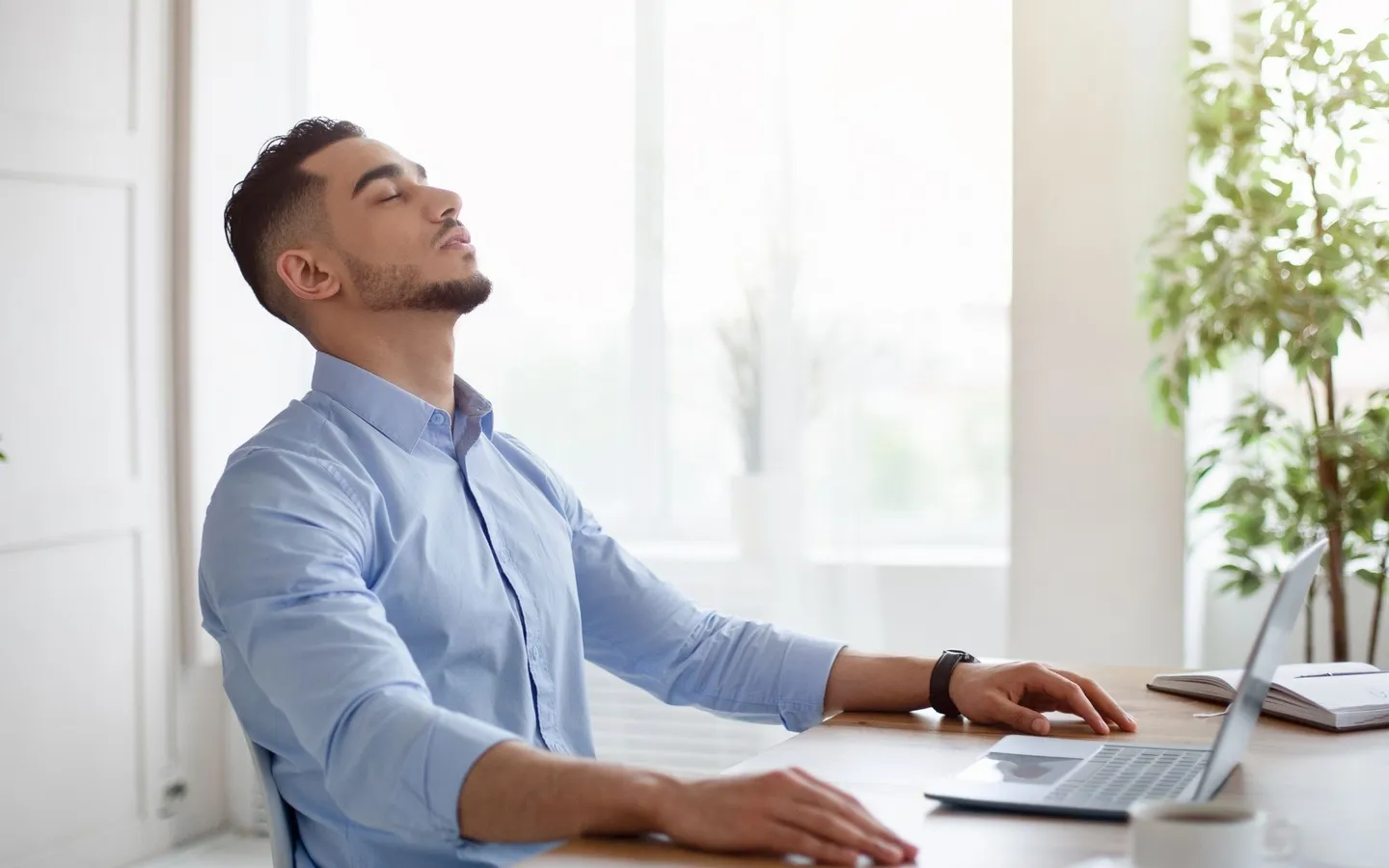 Un homme assis à son bureau, les yeux fermés et le visage tourné vers la lumière de la fenêtre, le temps d'une respiration.