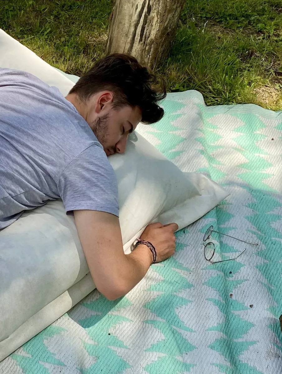 Une personne allongée sur un plaid, dehors, en train de dormir.