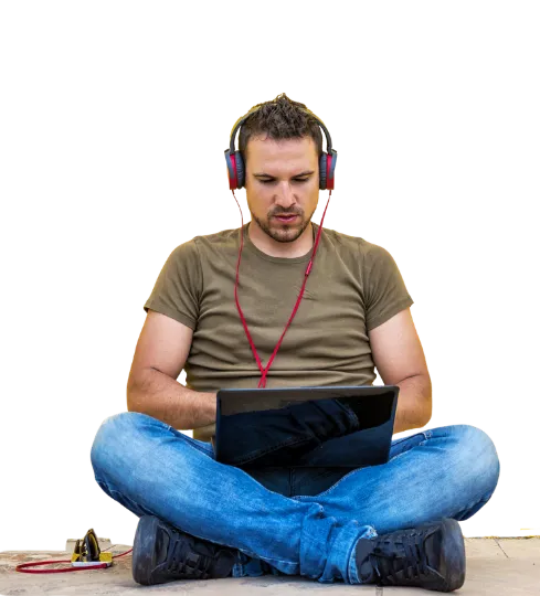 Un étudiant assis en tailleur, casque sur les oreilles, travaille sur son ordinateur portable.