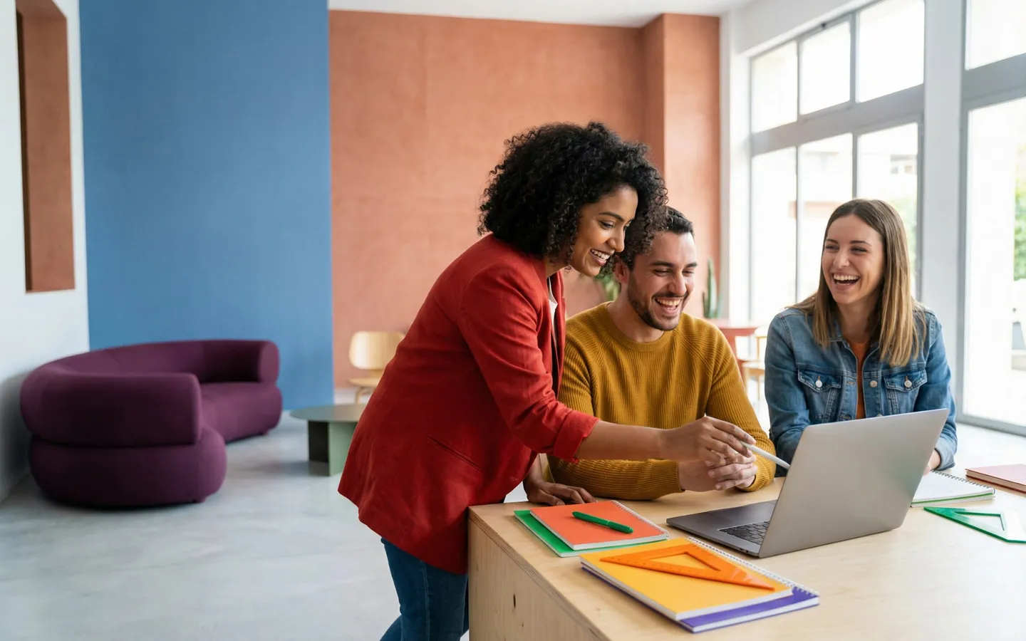 Trois collègues réunis autour d'un ordinateur portable dans un espace de travail coloré, en train d'échanger.